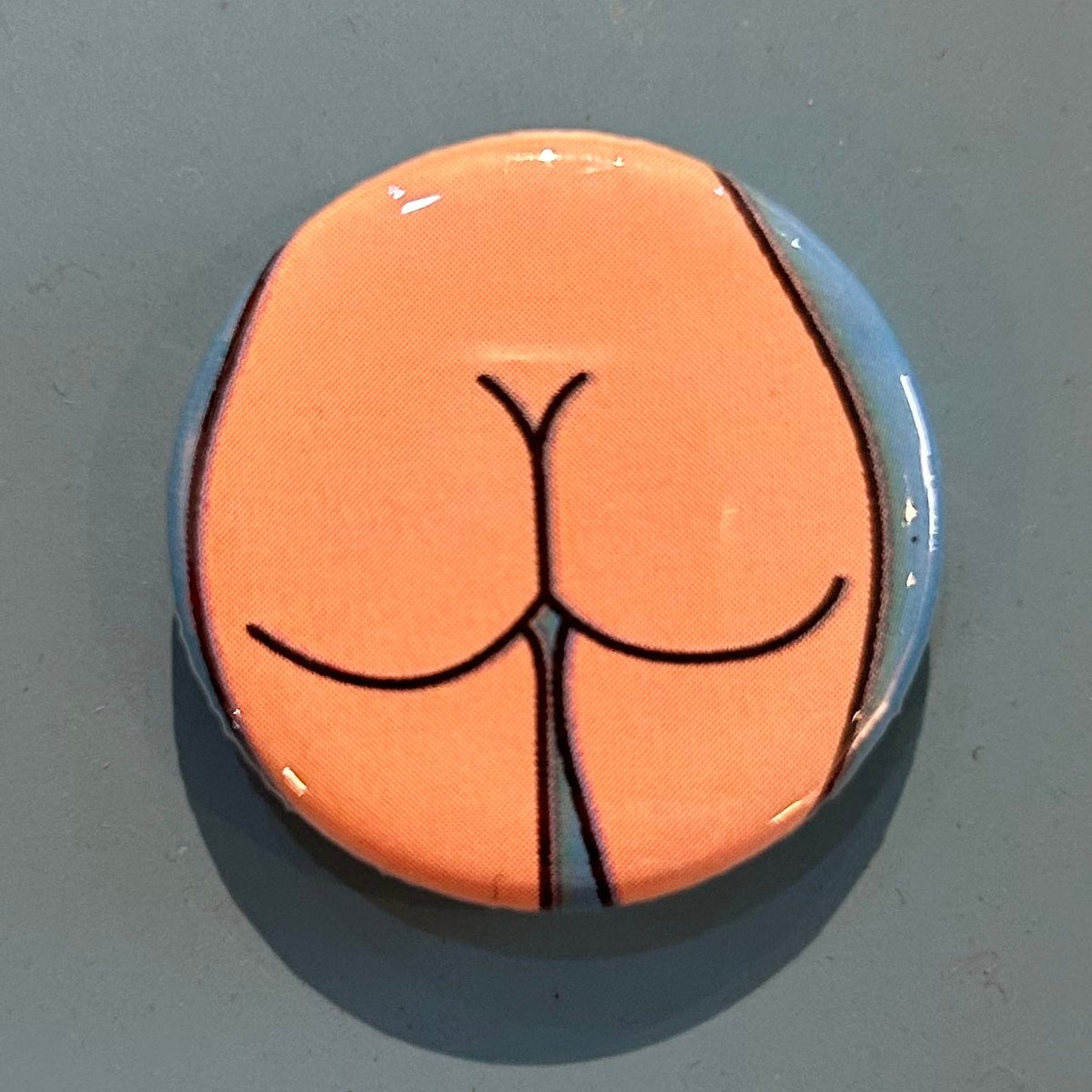 Round zipper pull with a round butt design on a gray background. 