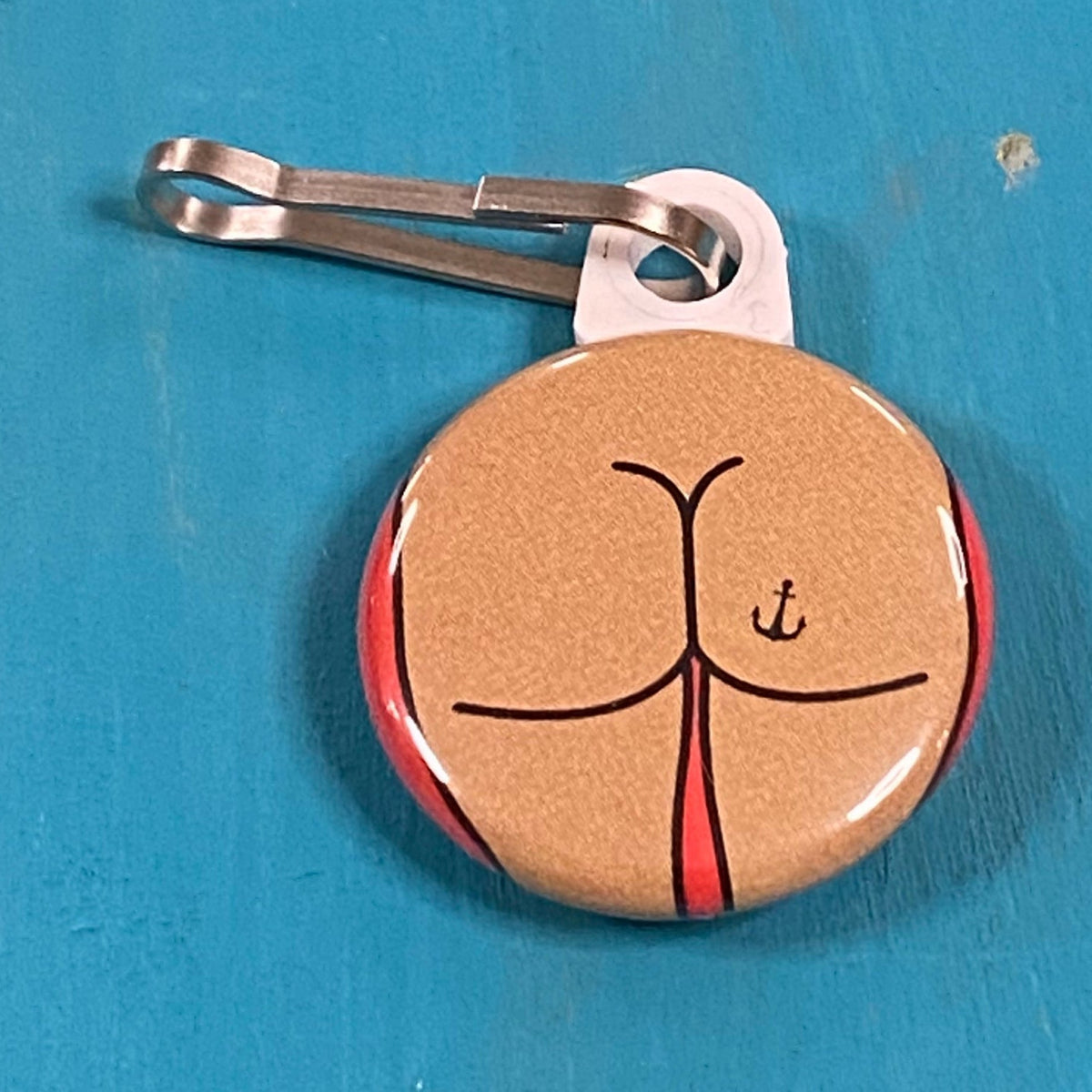 Round zipper pull with a square butt with an anchor tattoo on a blue surface. 
