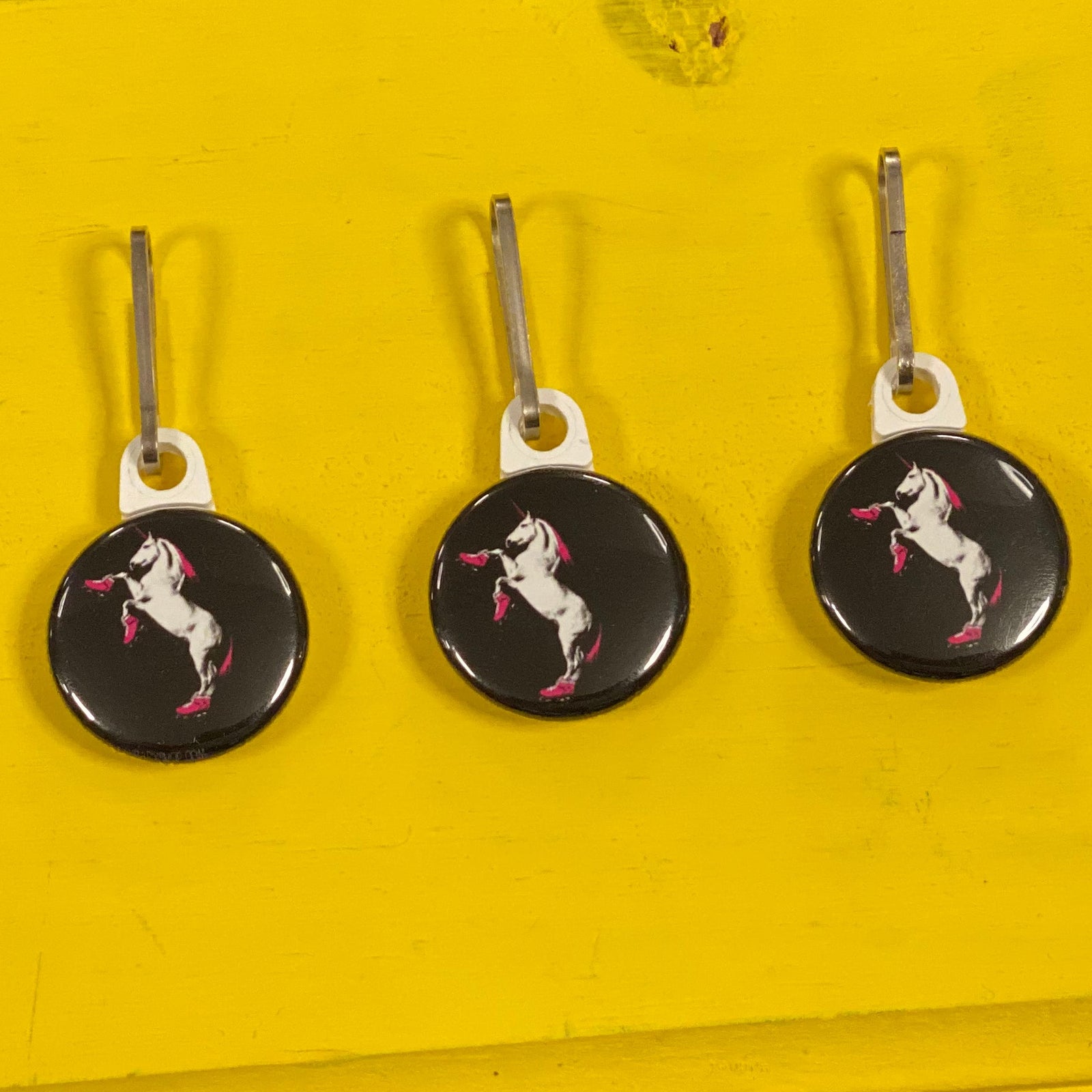 Three black zipper pulls with a roller skating unicorn design on a yellow wooden background