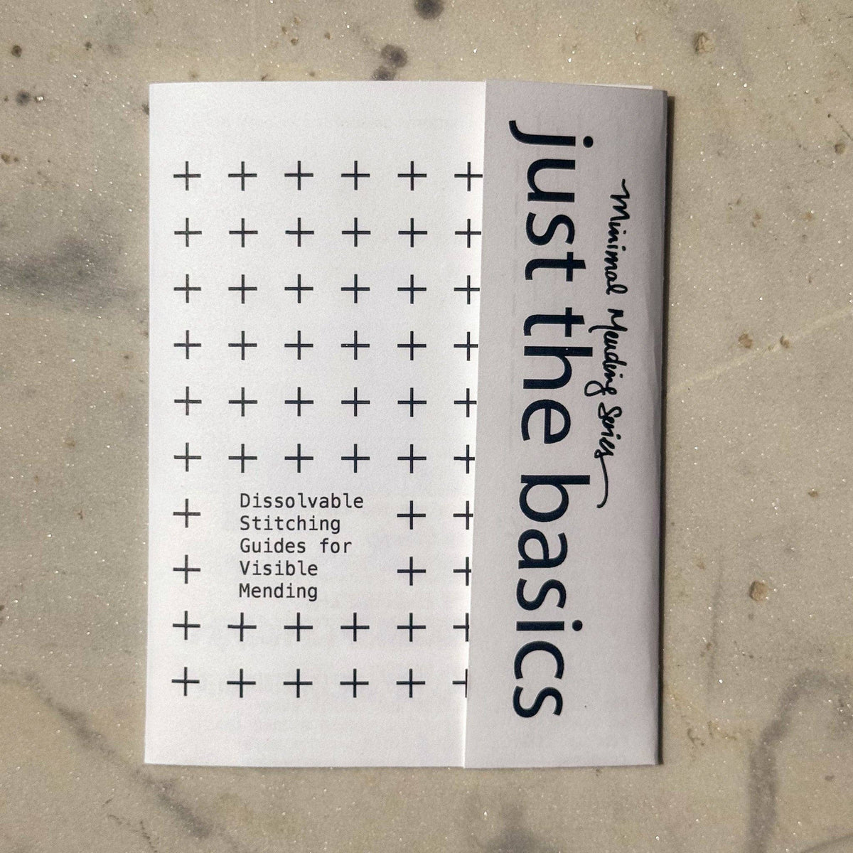 Booklet titled 'Just the Basics' with black text on a white background, lying flat on a textured surface.