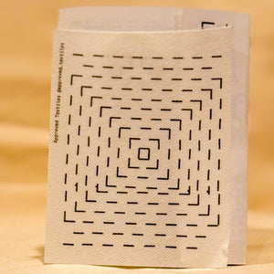 Visible mending guides sticker featuring concentric squares against a light yellow out-of-focus background. 