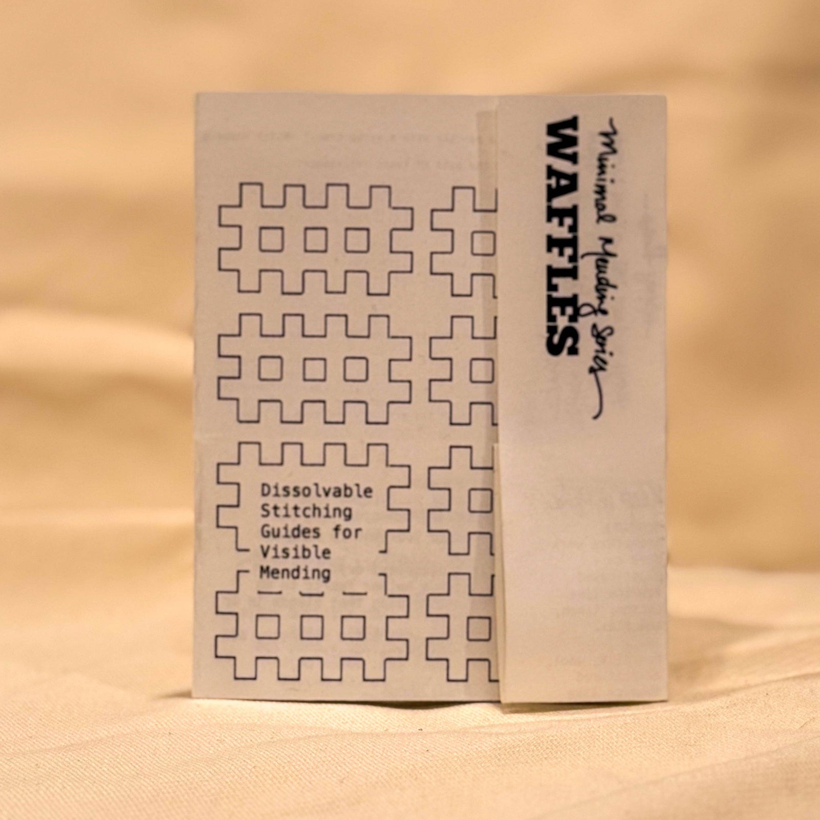 A small booklet titled 'Waffles' with sewing pattern diagrams, standing upright on a beige fabric surface.