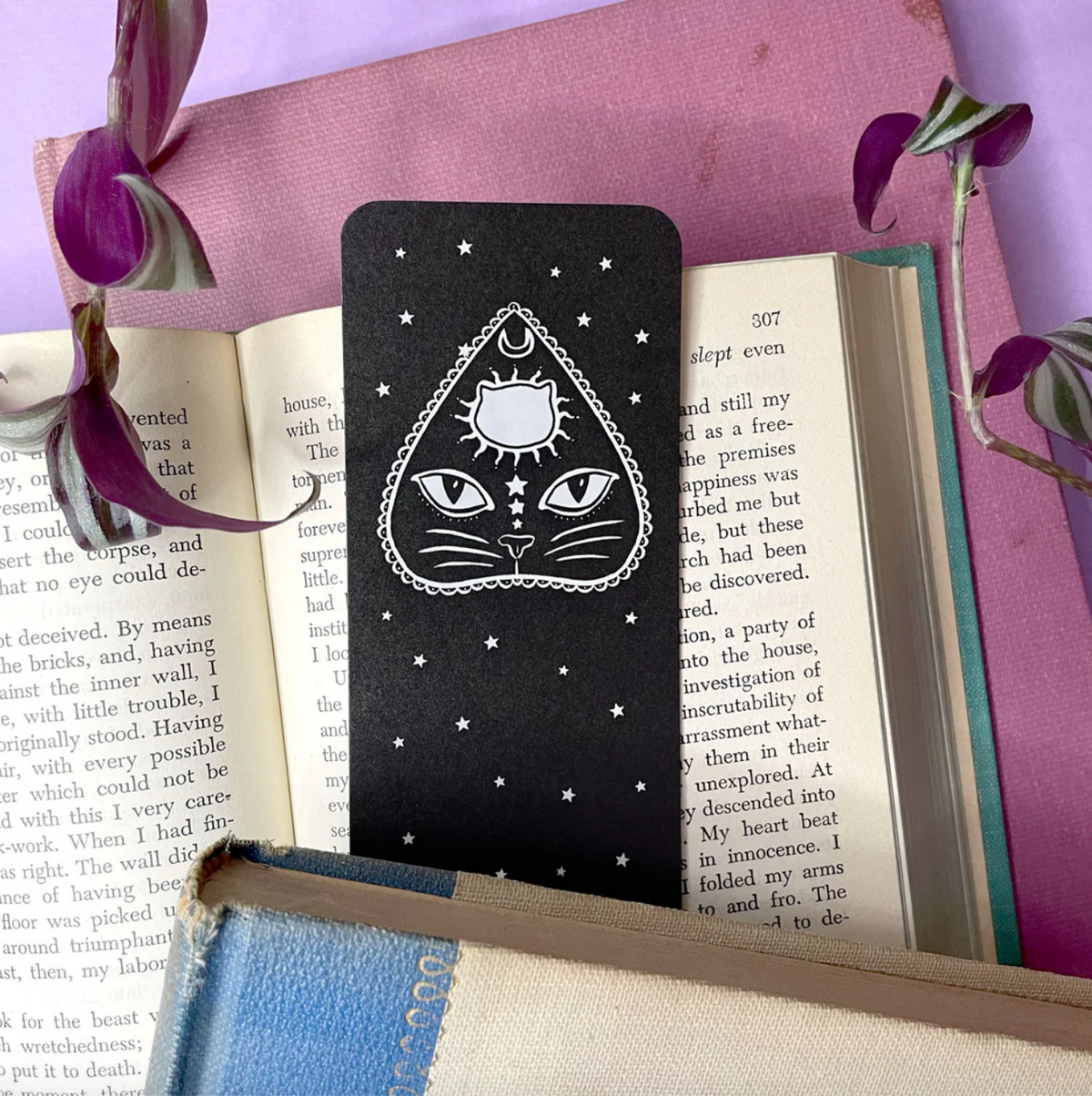 Black cat-themed bookmark on an open book with a purple background