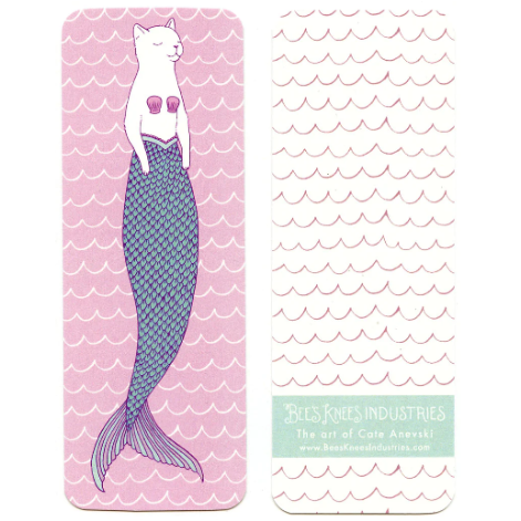 A bookmark that has a white cat wearing a shell bra with a mermaid tail on one side, and a pink scallop pattern against a white background on the other. 