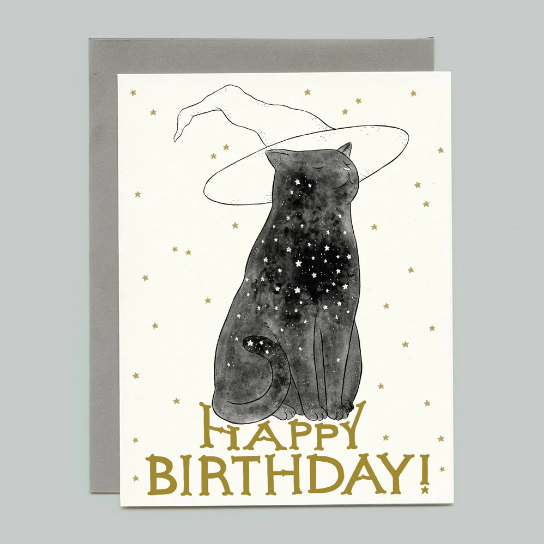 A card that says "Happy Birthday!" in gold writing and has an illustration of a black cat patterned with stars wearing a witch hat. 