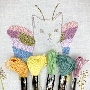 Embroidery of a cat butterfly with colorful floss skeins on a textured fabric background