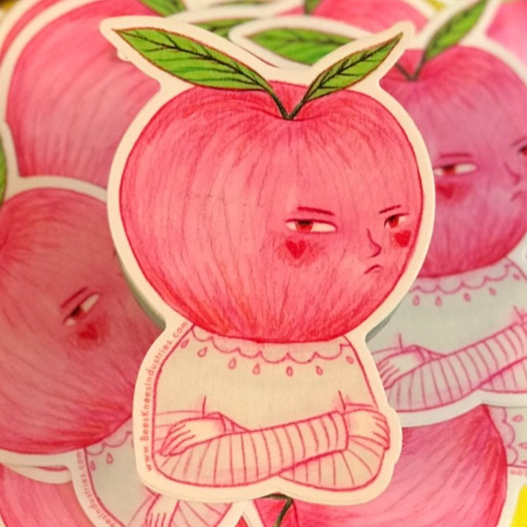 Sticker of an apple with a grumpy expression and a torso with crossed arms. 