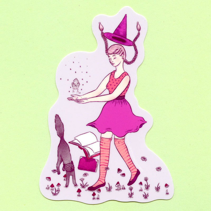 A sticker of a witch wearing a pink outfit levitating a crystal with a black cat and spell books.