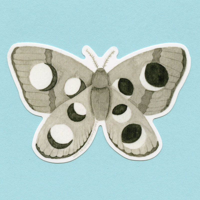 A sticker in various shades of gray of a moth with different phases of the moon on its wings. 