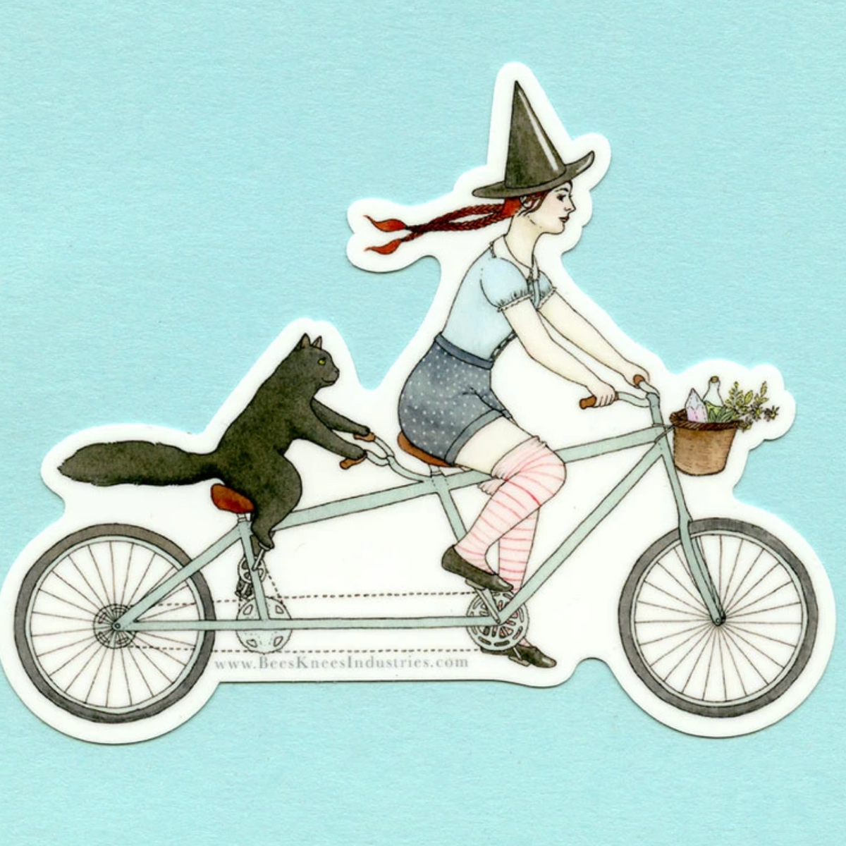 A sticker of a witch and her cat riding a tandem bicycle against a blue background.
