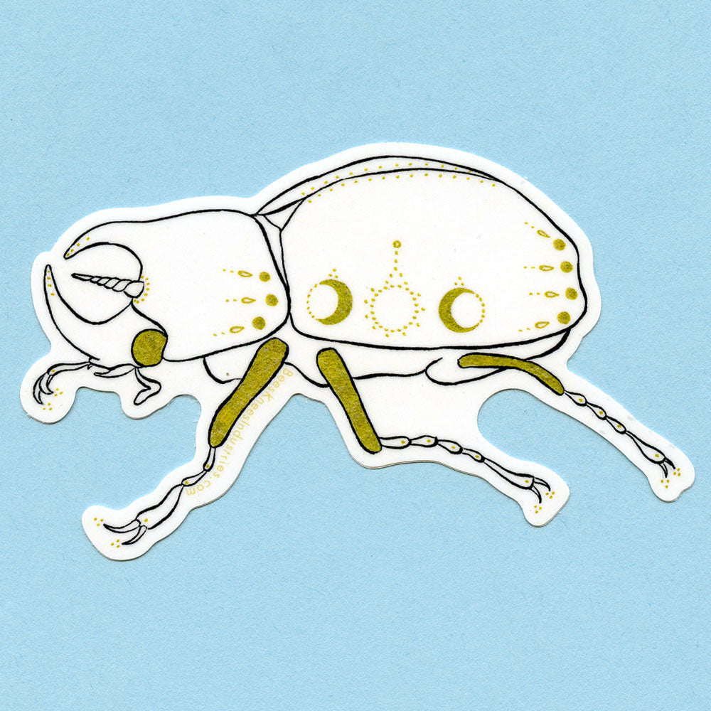 Black, white, and gold sticker of a beetle with a unicorn horn and sun and moon patterns on its body. 