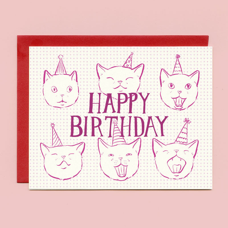 A card that says "Happy Birthday" and has drawings of cats wearing party hats against a pink background. 