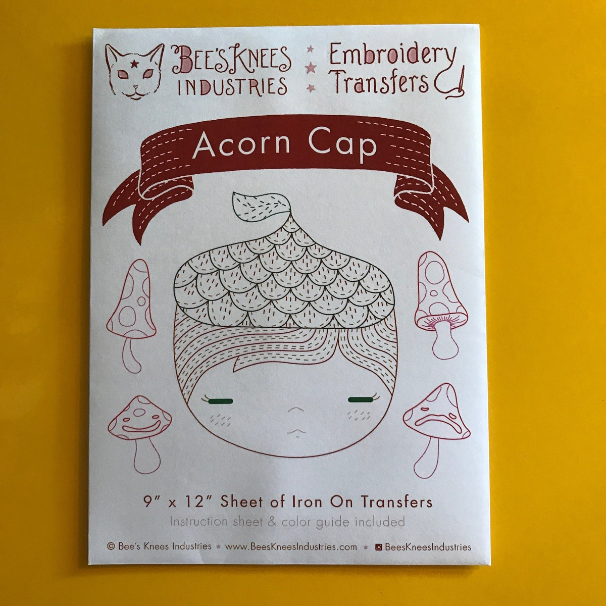 A paper envelope that says "Bee's Knees Industries Embroidery Transfers: Acorn Cap" and has illustrations against a yellow background. 