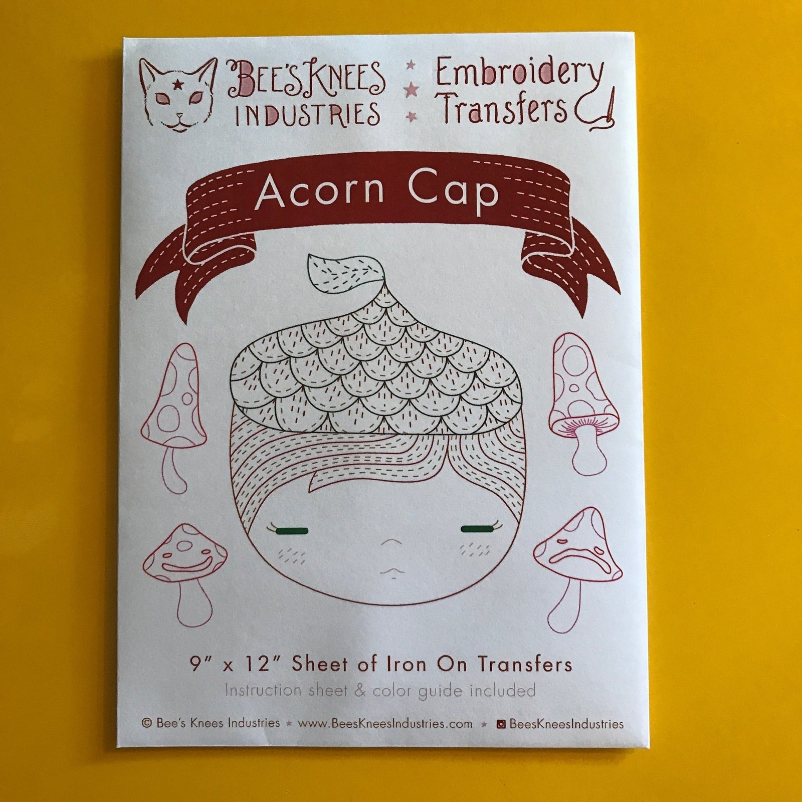 A paper envelope that says "Bee's Knees Industries Embroidery Transfers: Acorn Cap" and has illustrations against a yellow background. 
