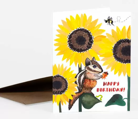 This birthday card shows a chipmunk sitting on a sunflower leaf. He is holding an acorn and a bee is buzzing around the top. The card says Happy Birthday.