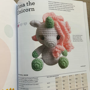 An open craft  book page featuring a crocheted amigurumi unicorn named 'Uma the Unicorn,' with printed text, yarn color notes, and a small yarn measurement chart.