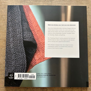 The back cover of a bookphotographed flat on a wooden surface. The cover features a close-up of a knitted dog design in black, rust red, and light blue, with a white text box containing product descriptions and a barcode at the bottom.
