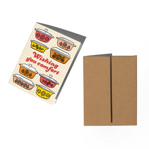 Greeting card with colorful illustrations of pots and pans and 'Wishing you comfort' text, next to a brown envelope.