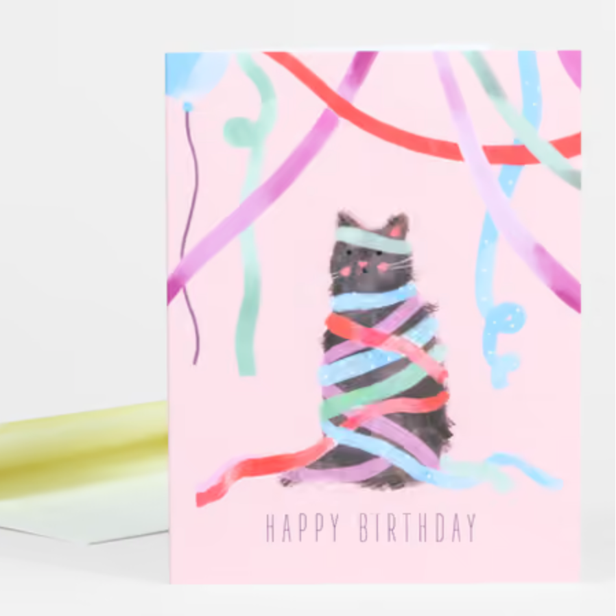 A pink card featuring a black cat wrapped up in party streamers and the text "Happy Birthday" at the bottom