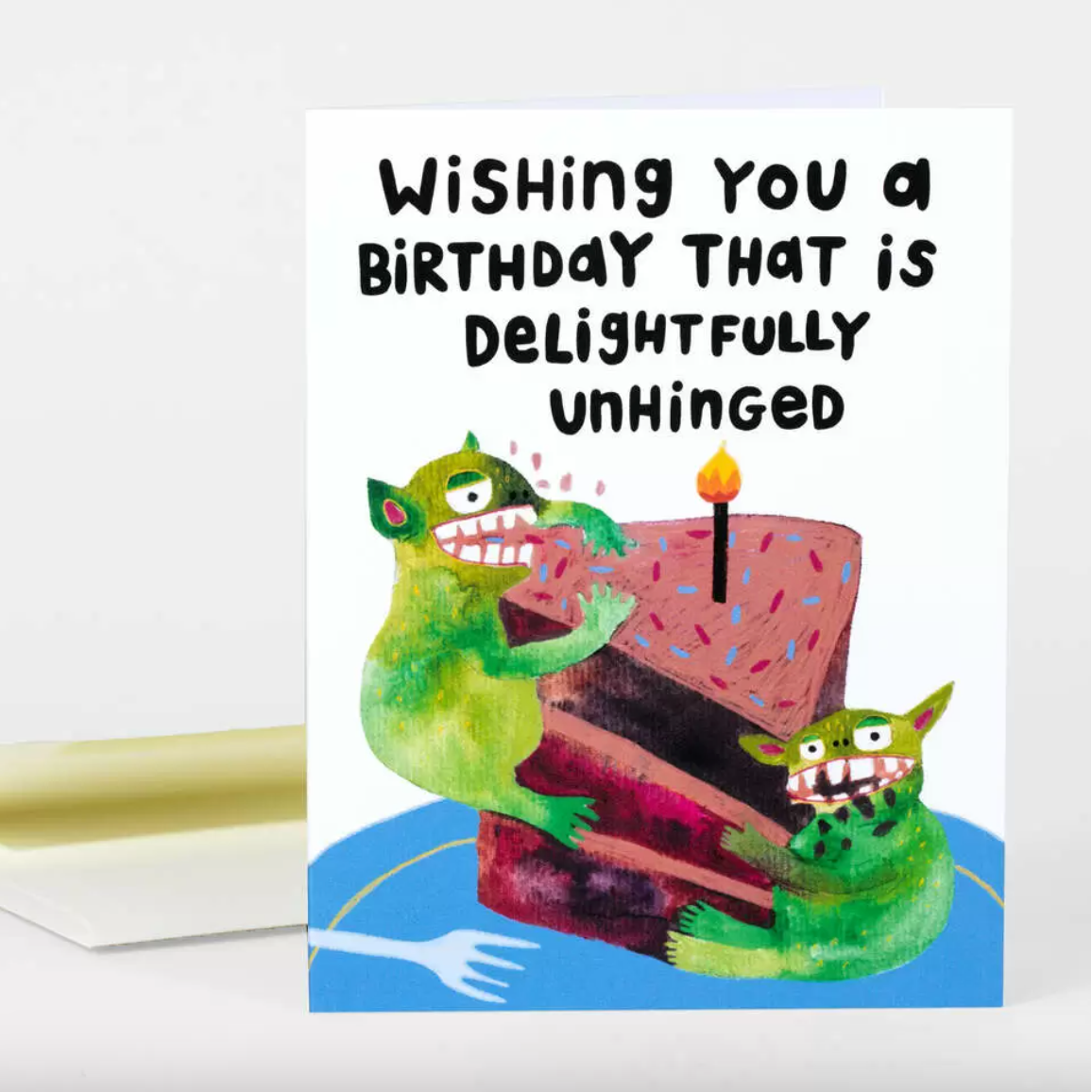 A birthday card with two green gremlins eating a slice of cake and text above that says "Wishing you a birthday that is delightfully unhinged"