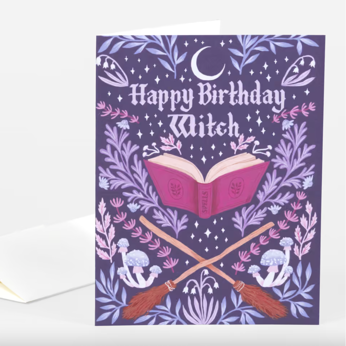 A dark purple card with a crescent moon, leaves and mushrooms, a spellbook, two brooms crossed at the handles, and text that reads "Happy Birthday Witch"