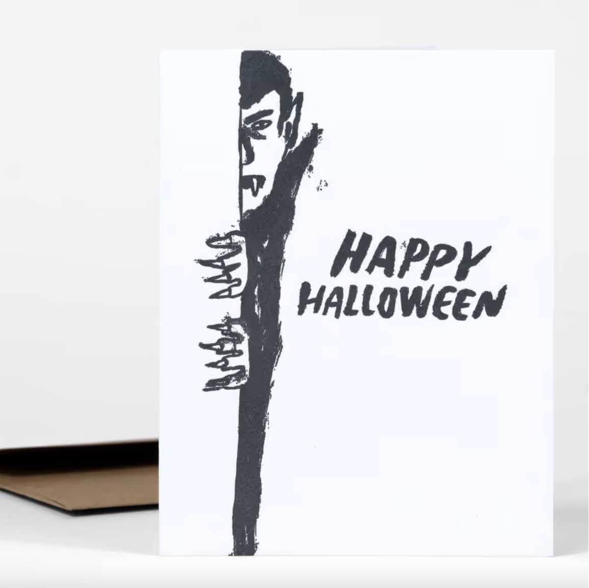 A white card with a black illustration of Dracula peeking around a corner and text that reads "Happy Halloween"