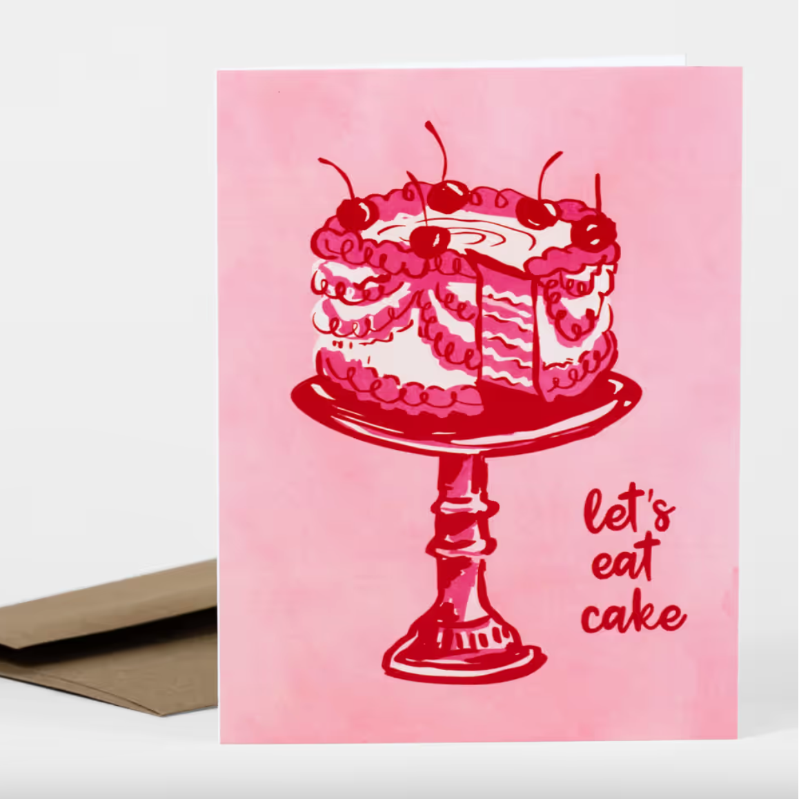 A pink card featuring a birthday cake on a cake stand and red script that says "let's eat cake"