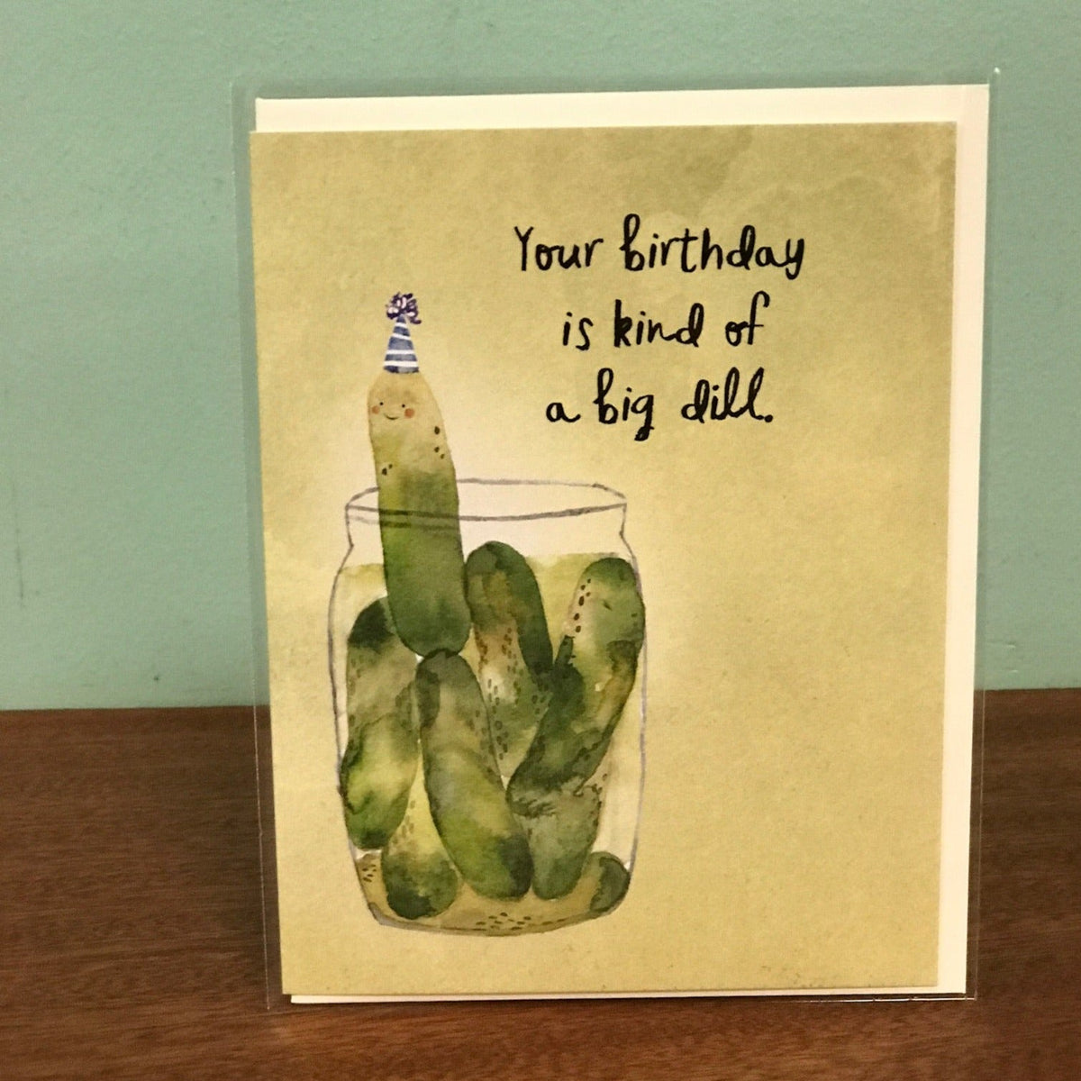 Birthday card with pickle illustration and humorous text on a wooden surface.