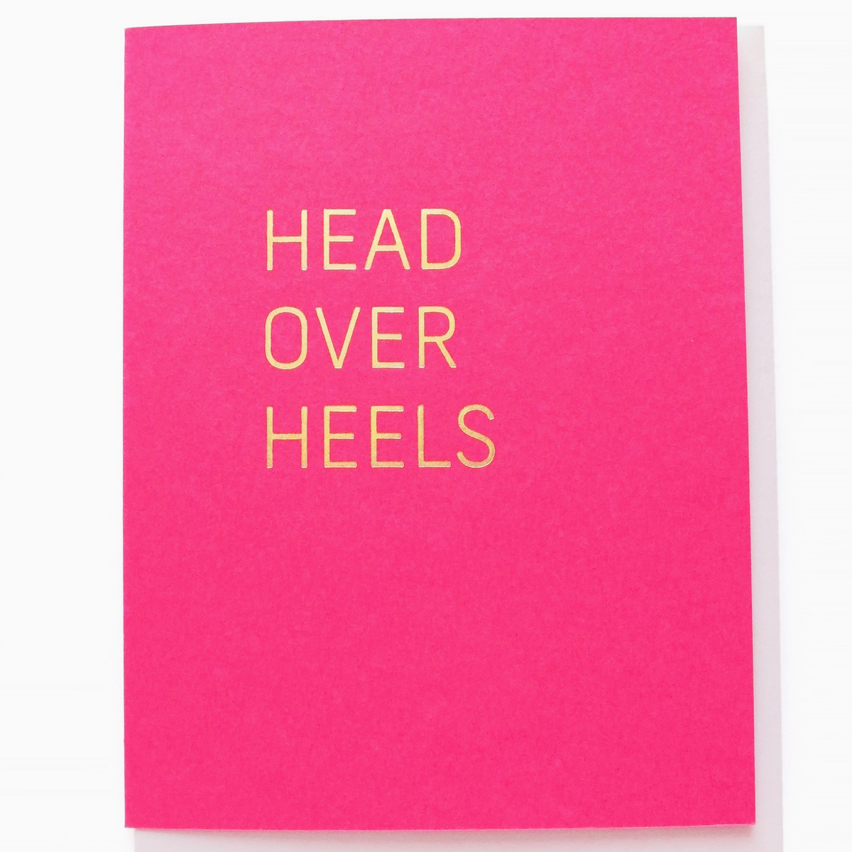 Pink card with 'HEAD OVER HEELS' text on a white background