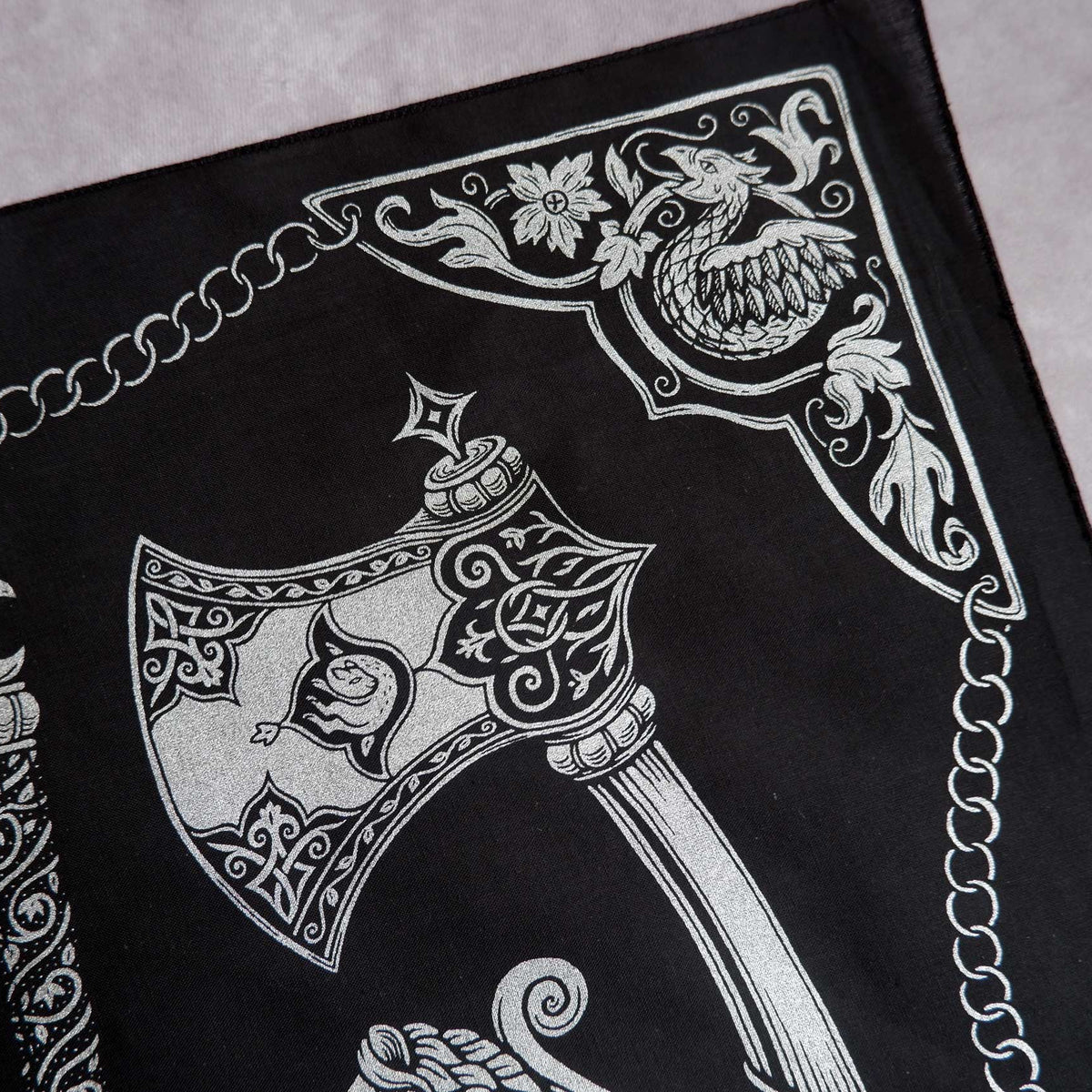 Close up of a decorative black fabric bandana with white intricate design featuring an axe and floral elements.