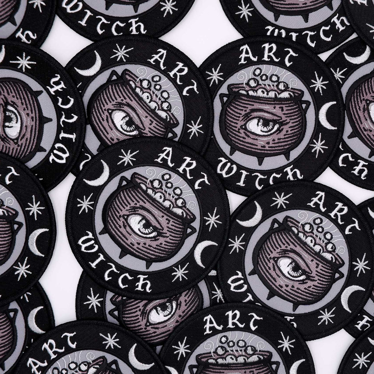 A grouping of circular patches that feature stars, crescent moons, a cauldron with an eye on it in the center, and text that says "Art Witch"