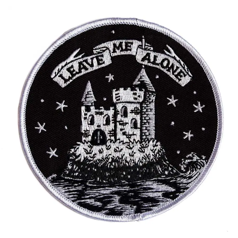 A round embroidered patch featuring a castle on an island surrounded by water and stars and the text "LEAVE ME ALONE" on a banner above