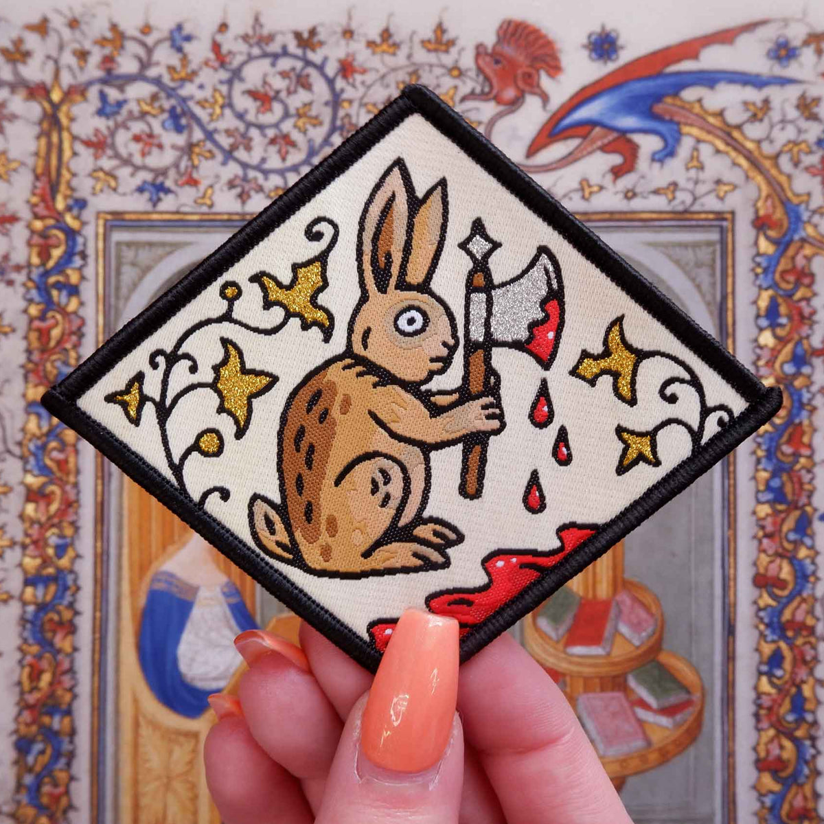 Embroidered patch of a rabbit holding an axe with decorative border held by a hand.
