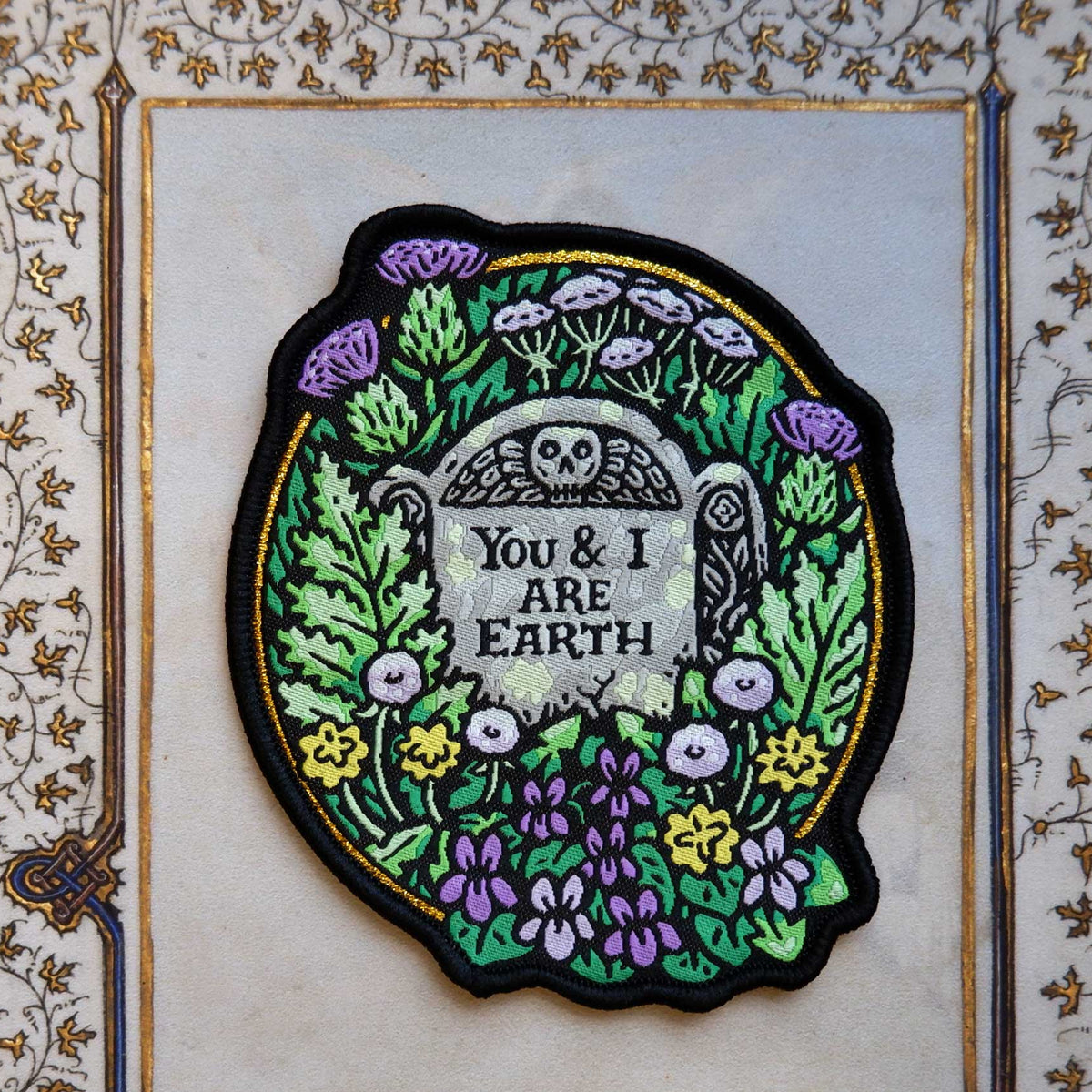 Embroidered patch with floral design and text that says "You and I are earth" on a decorative background