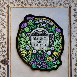 Embroidered patch with floral design and text that says "You and I are earth" on a decorative background