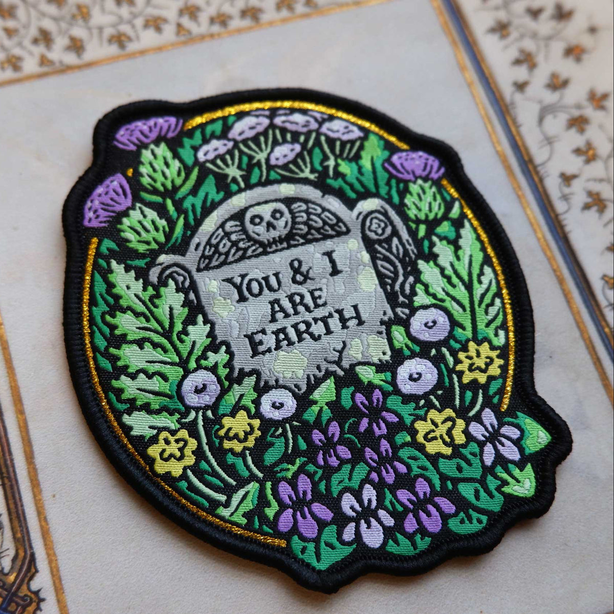 Embroidered patch with tombstone design and floral elements on a decorative background