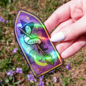 Holographic worm witch design on a sticker held by a hand with a blurred natural background