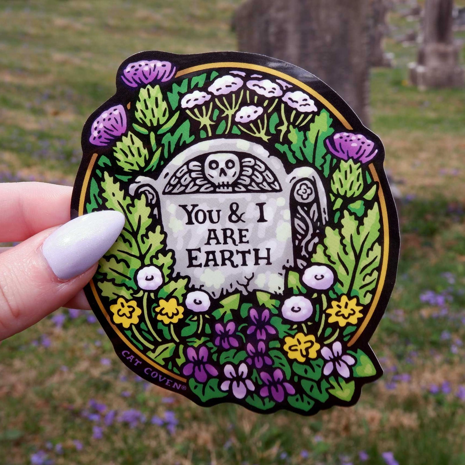 Decorative sticker with 'You & I Are Earth' text held in front of a natural background