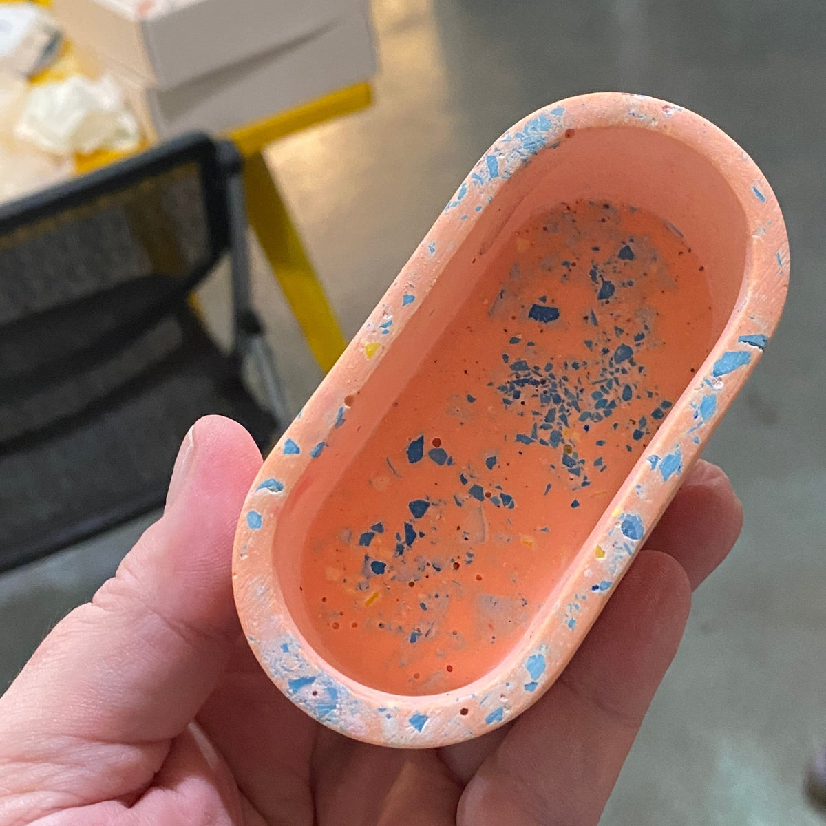Hand holding an oval, orange terrazzo container (business card holder) with blue specks.
