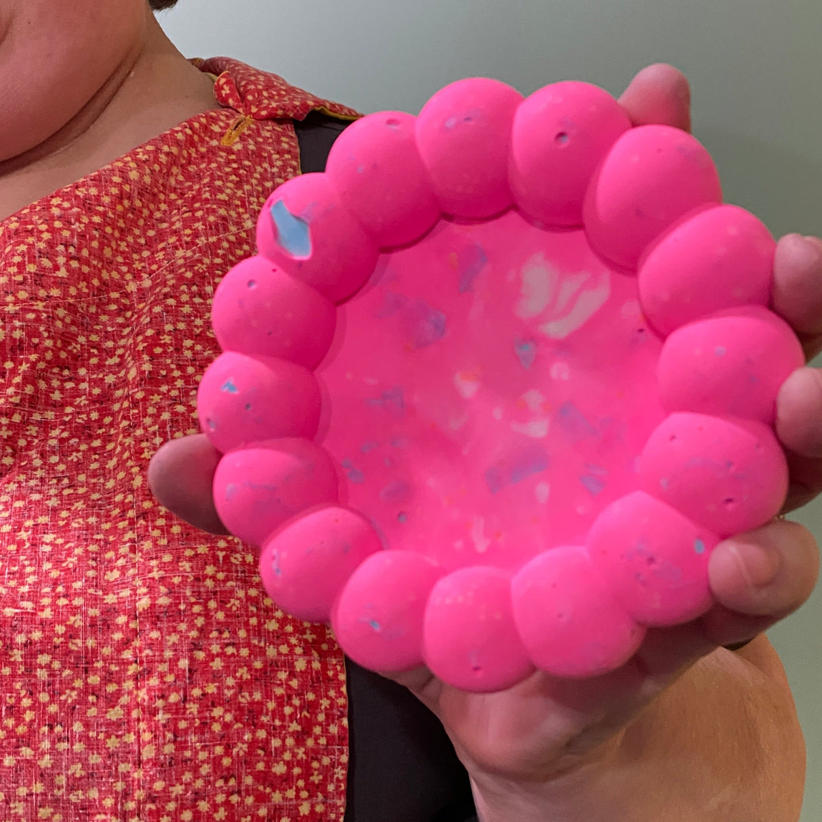 Person holding a pink dish against a neutral background.