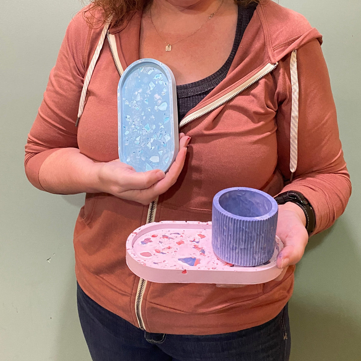 Woman holding a tray with a blue container and a pink lid against a plain background.