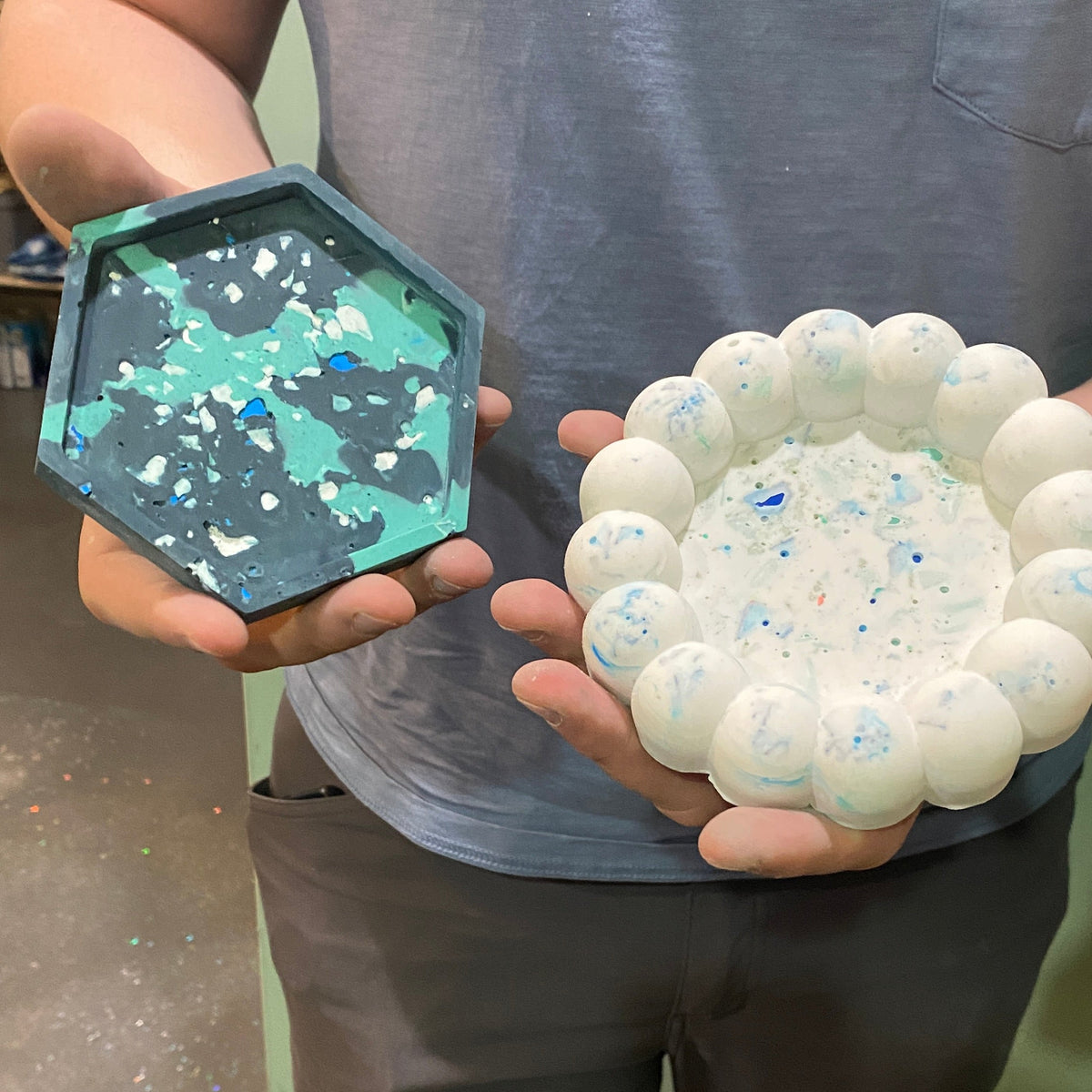 Person holding two decorative items, one green and one white, against a neutral background.