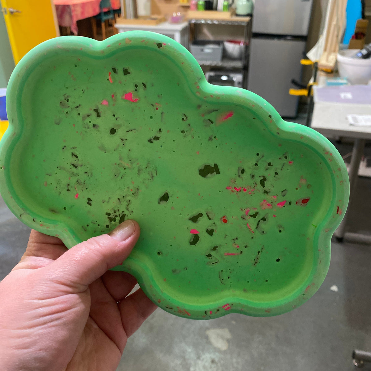 Green textured plate held by a hand in an indoor setting.