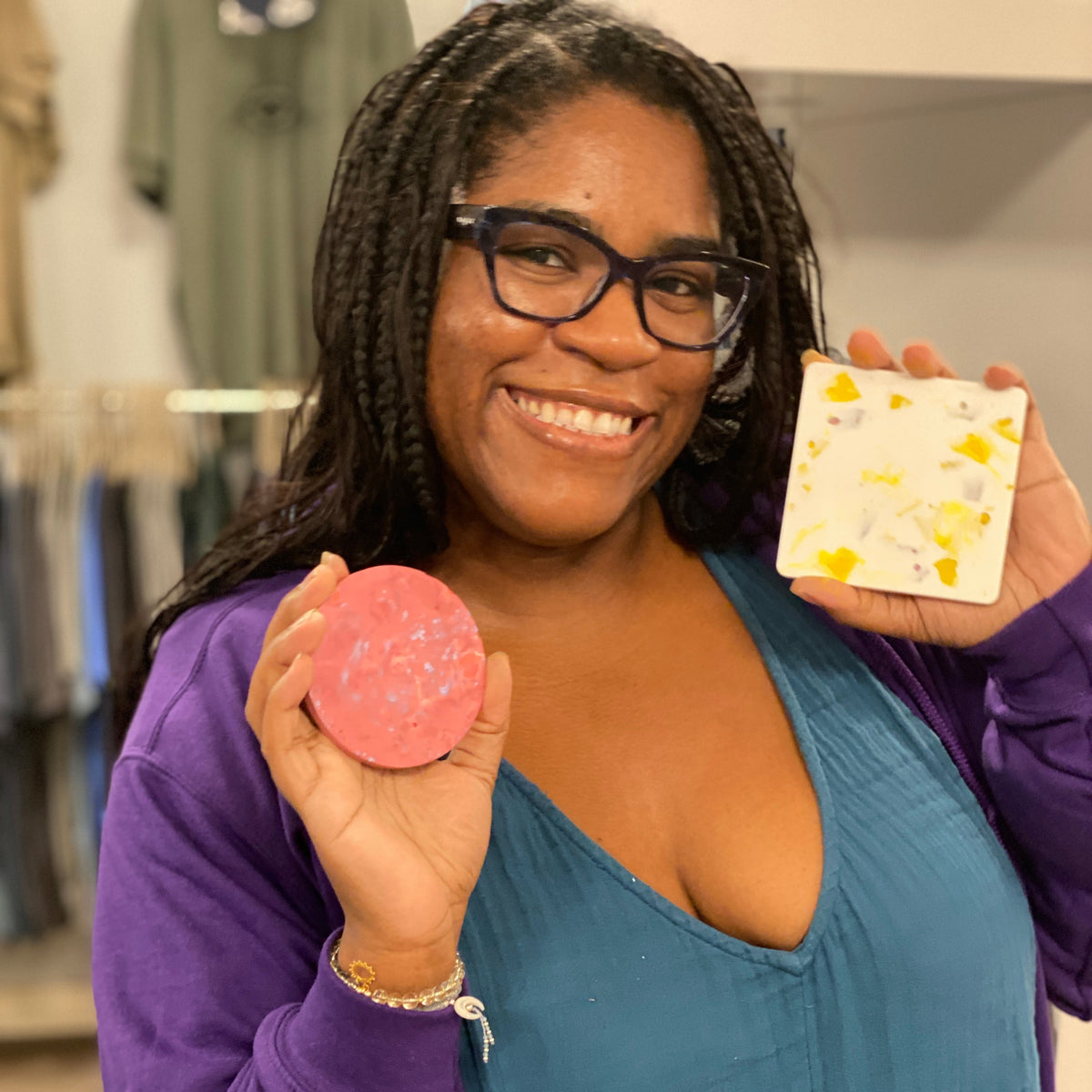 Woman holding two coasters, one pink and one with yellow patterns, in a store setting.