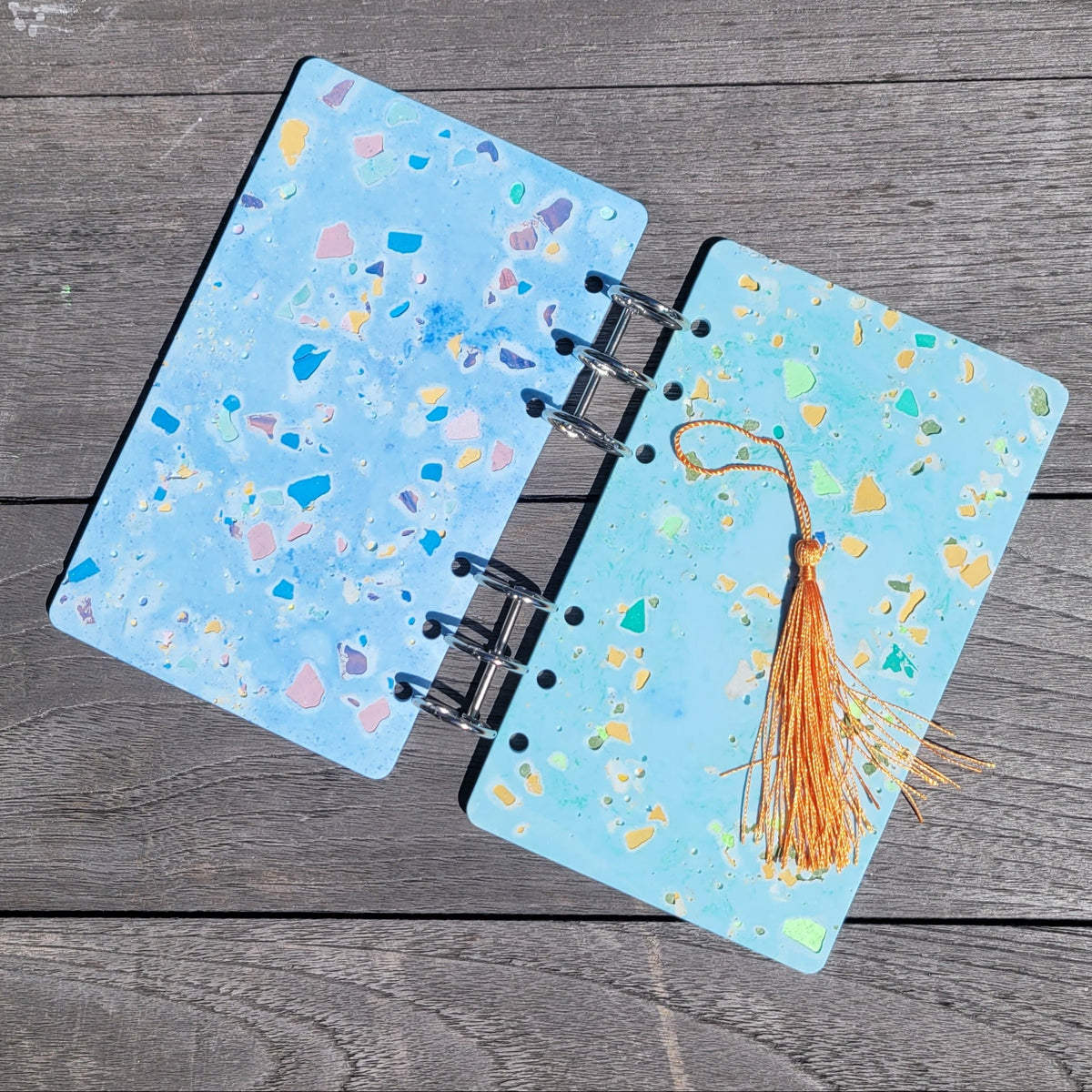 Open notebook with terrazzo design and a tassel on a wooden surface. 