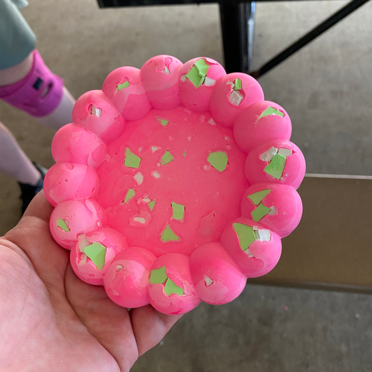 Pink textured dish with green accents held in a hand against a neutral background.