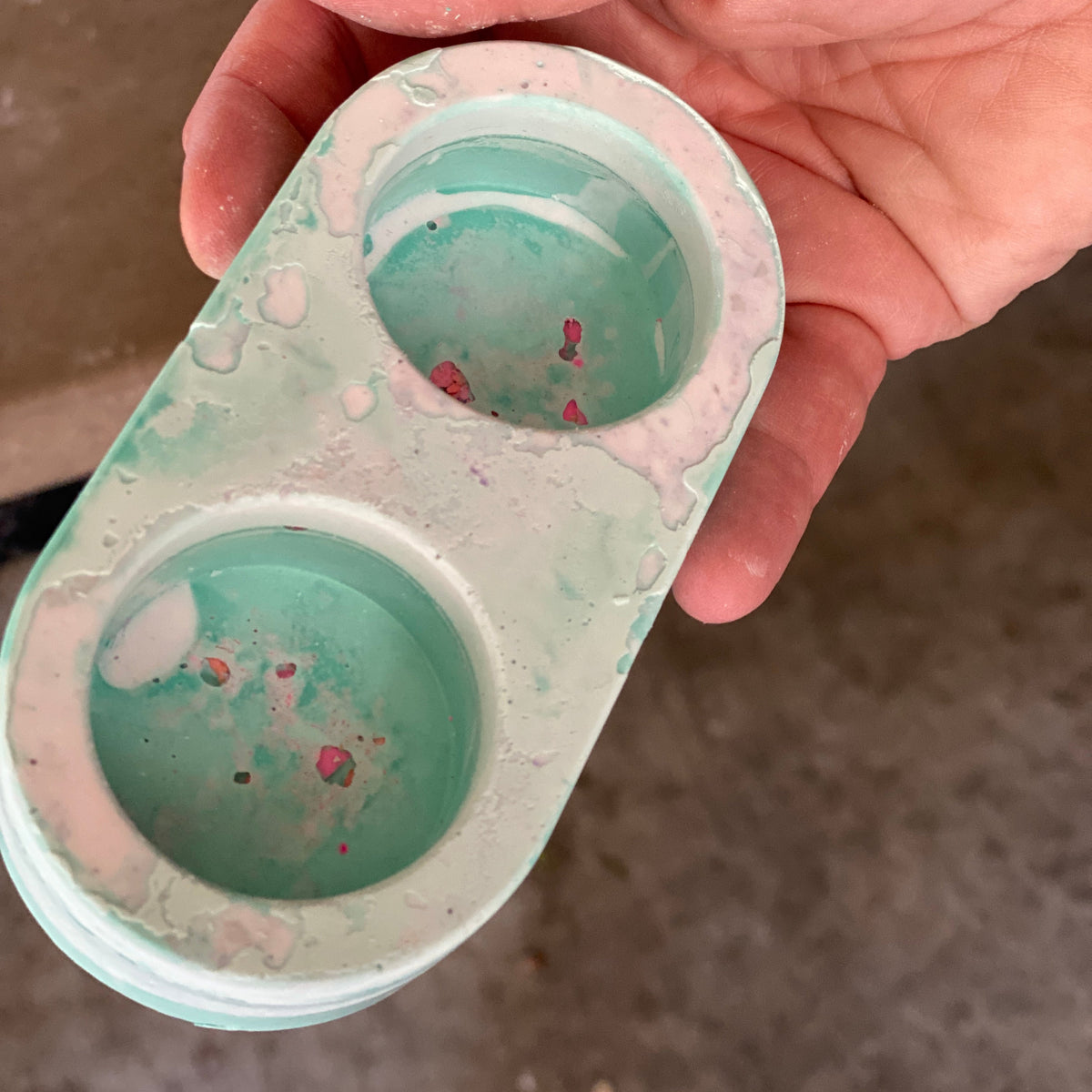 Hand holding a green terrazzo candle holder with two circular cavities.