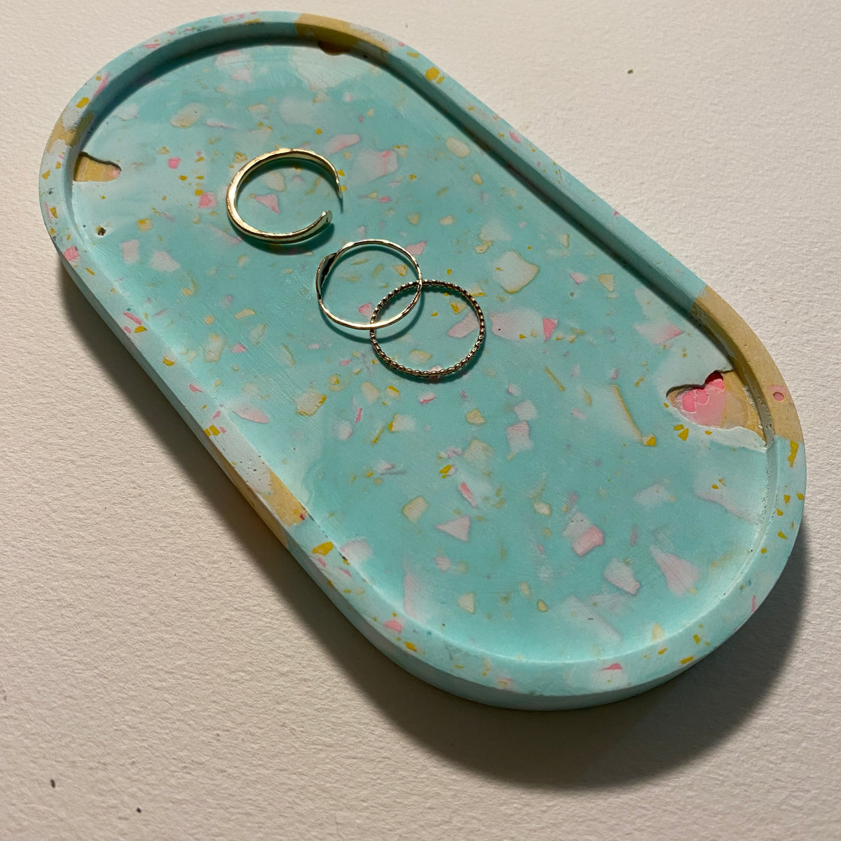 Decorative tray with colorful speckled terrazzo pattern holding three rings on a beige background.