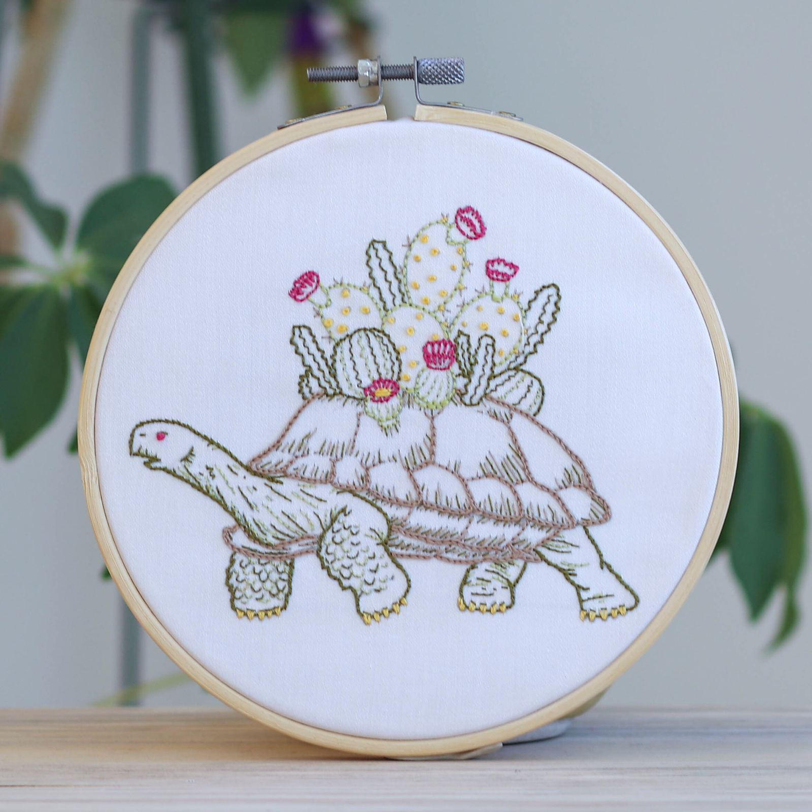 Embroidery hoop with a turtle and cactus design on white fabric.