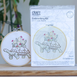 Embroidery kit with turtle design and packaging on a wooden surface.